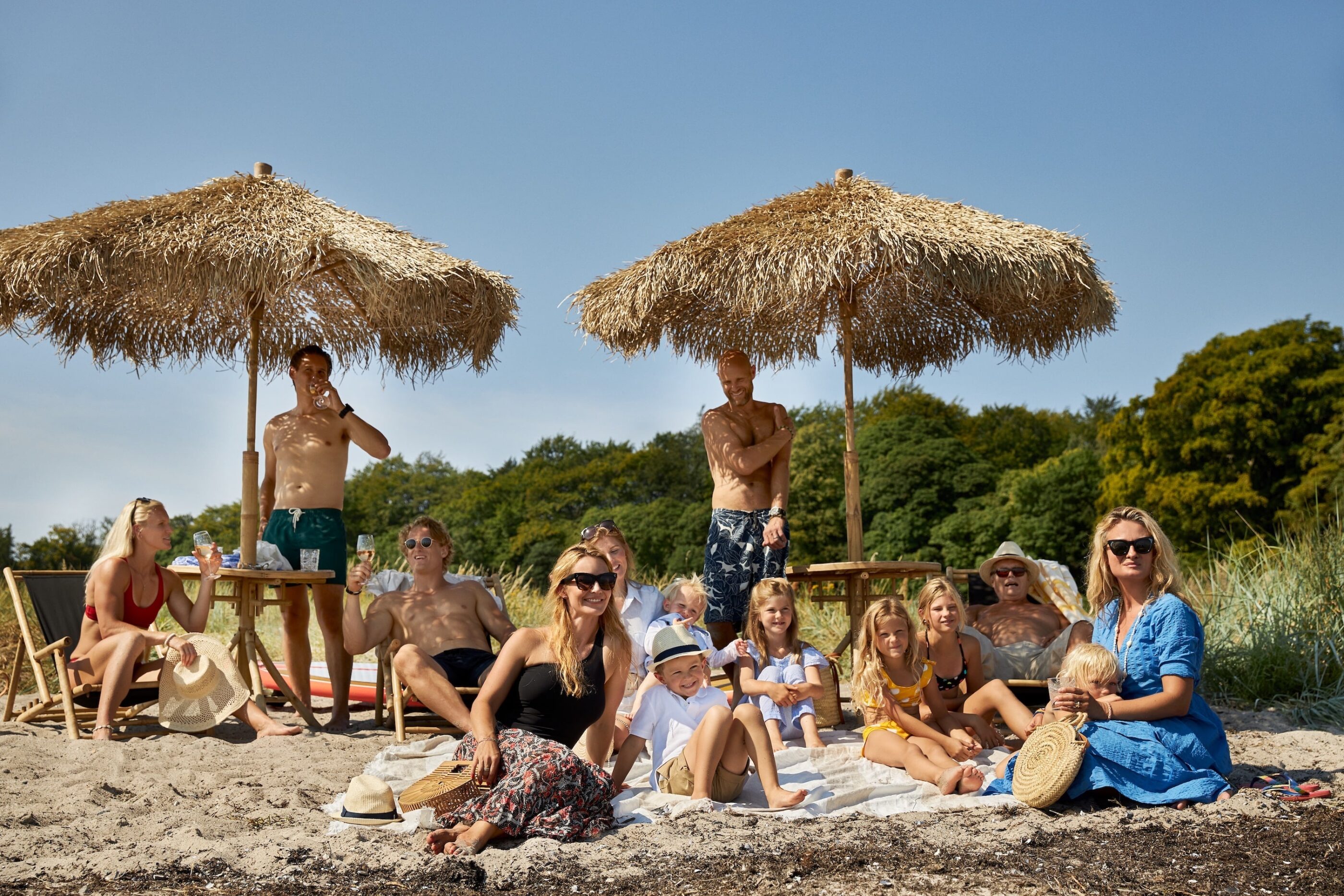 Flere mennesker er samlet på en strand, både børn og voksne, som begge smiler af noget i horizonten