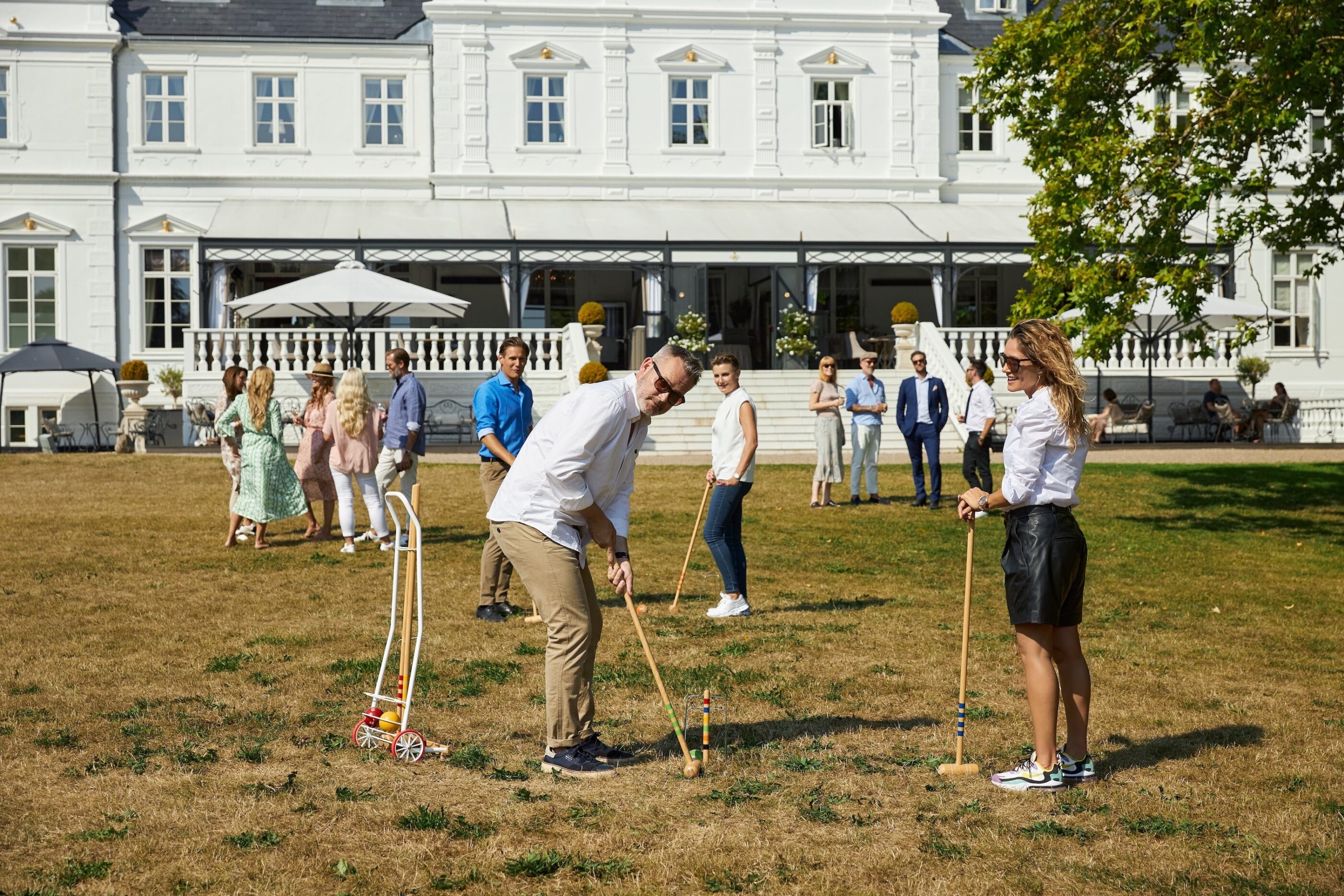 4 mennesker spiller Kroket i hotellets have med hotellet og resten af deres gruppe i baggrunden