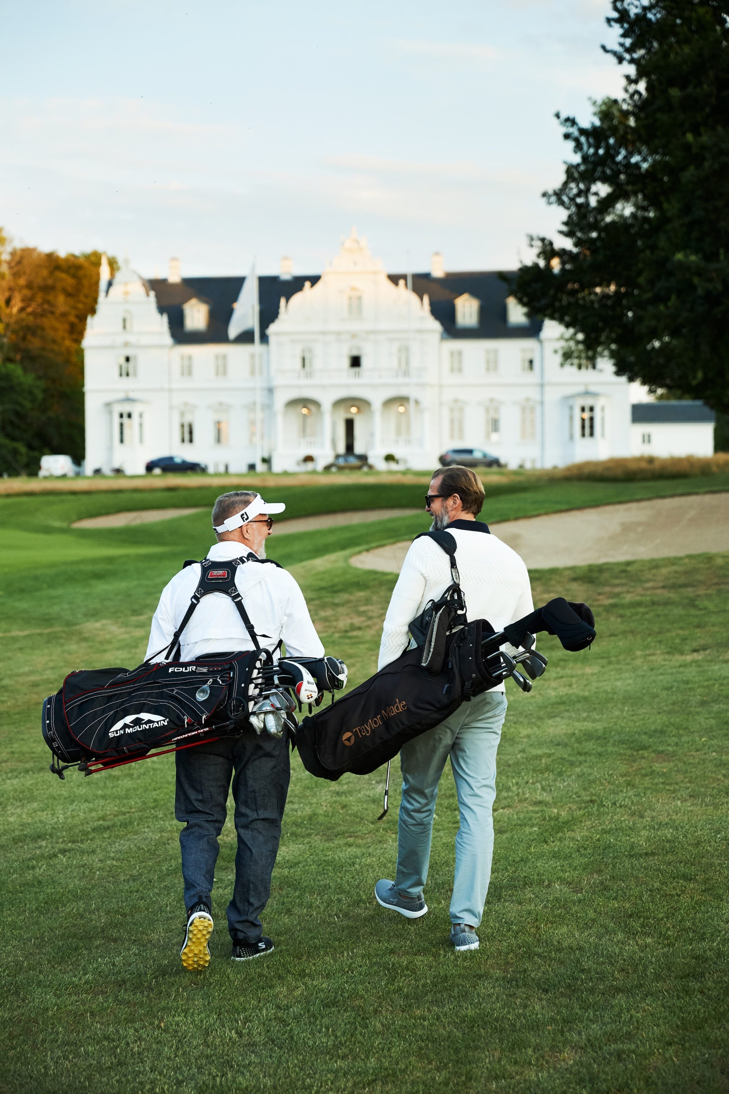 2 mænd går ned af golfbanen med golftasker i armen med udsigt til hotellet i foregrunden