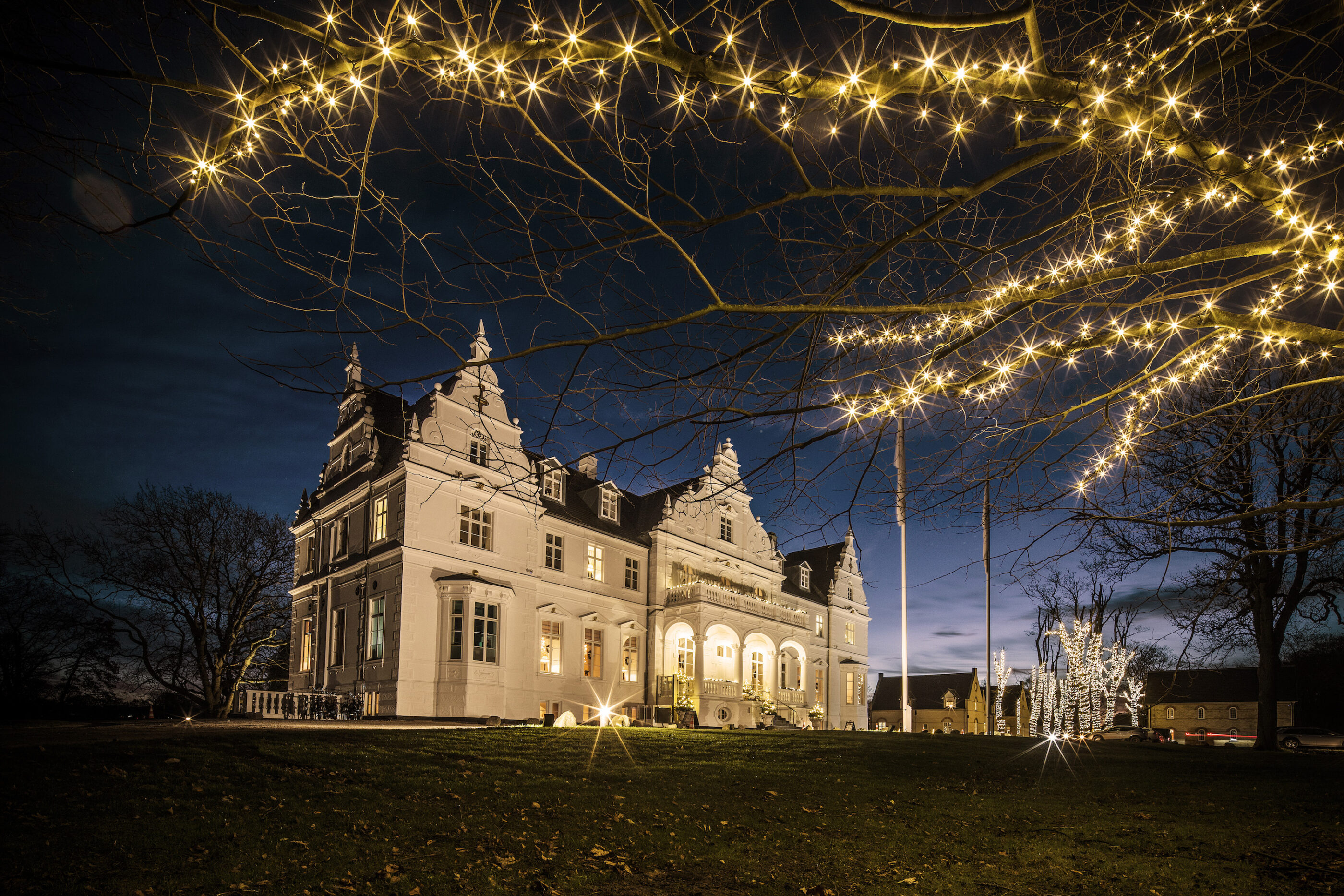 Kokkedal Slot om natten med julelys dekoreret på træerne foran slottet