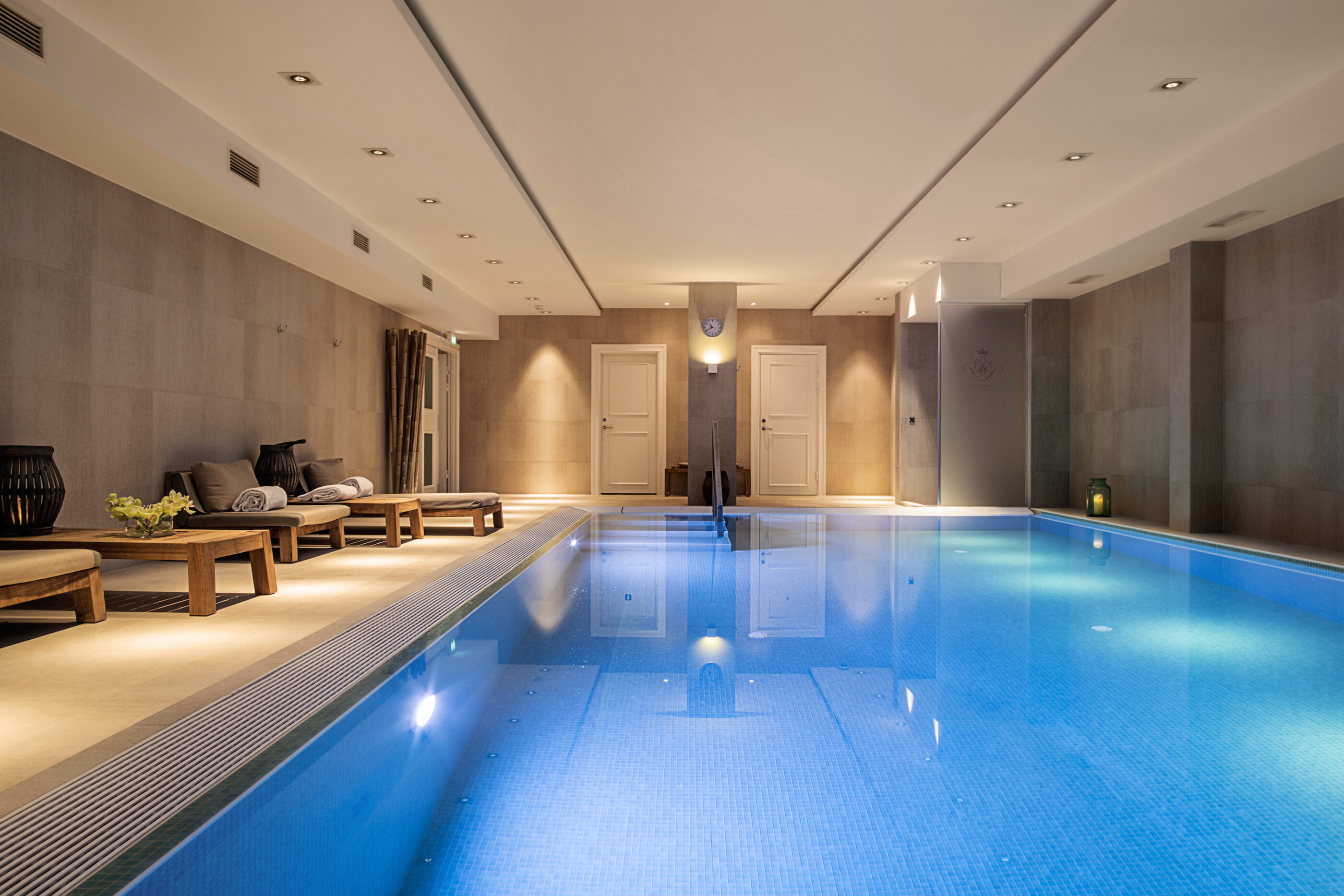 Infinity pool med hyggelig indendørsbelysning og liggestole med håndklæder